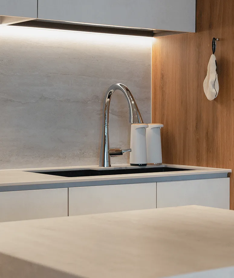 Close view of a pale stone sink and splashback with warm timber cabinetry